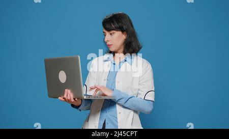 Microbiology chemist doing research work on laptop in studio, browsing internet to find chemical results and analysis. Chemistry scientist with white coat using computer experiment. Stock Photo