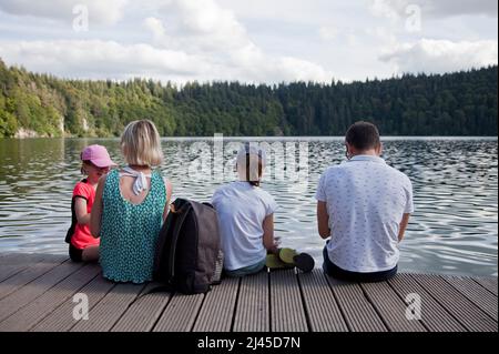 Besse-et-Saint-Anastaise (central France): family seated by Lake Pavin, volcanic lake of the Sancy Massif, in the Massif Central mountain range Stock Photo