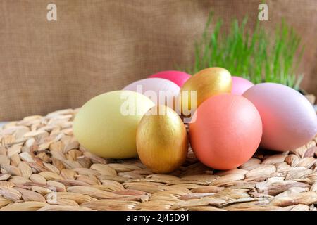 Easter colorful eggs in a basket on white wooden table. Burlap background. Happy Easter. Rustic, Eco concept. Dyed Eggs on a straw Napkin. Stock Photo