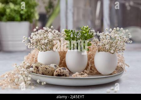 Easter composition. White eggs with funny faces painted on the table. A small bouquet in an egg. The minimal concept of Easter. An Easter card with a Stock Photo