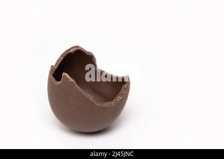 Cracked chocolate Easter egg on a white background, copy space. Half broken milk chocolate egg. Chocolate Easter concept. Stock Photo