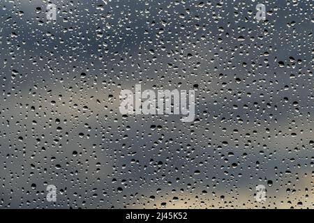 raindrops on a window pane with blurred dark clouds in the background Stock Photo
