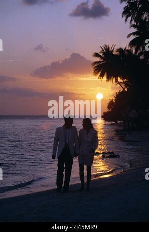 Maldives. Young couple in evening clothes, walking on beach at sunset. Stock Photo