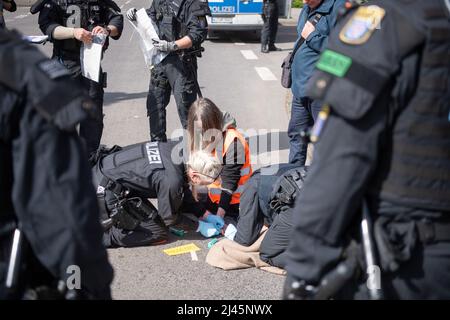 12 April 2022, Hessen, Frankfurt/Main: Police officers loosen the hand of a demonstrator during a protest of the group 'Last Generation'. He had stuck himself to the roadway with superglue. The group is calling for an immediate halt to all investment in and new expansion of fossil fuel infrastructure. Photo: Sebastian Gollnow/dpa Stock Photo