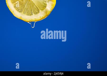 Fresh slice of lemon juice drip on blue background, citrus dripping isolated, copy space. Stock Photo