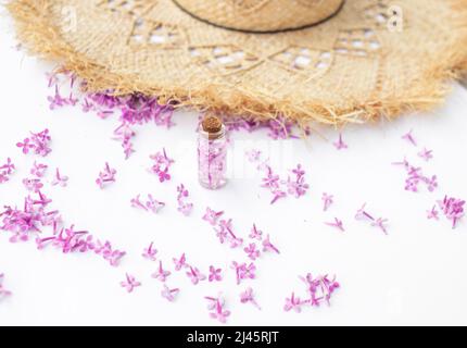 Transparent bottle with lilac flowers standing near a straw hat on a white background Stock Photo