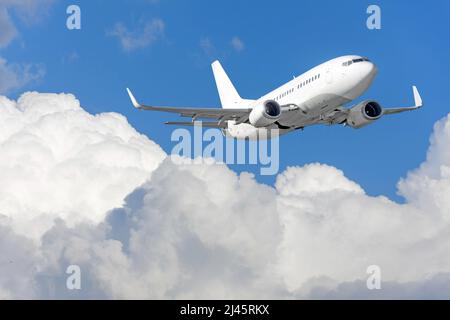 Climbing plane flies over the tops of cumulus clouds in the blue sky Stock Photo
