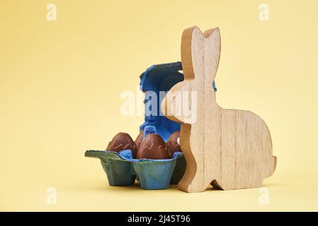 Wooden rabbit and chocolate eggs on yellow background, Happy Easter card Stock Photo