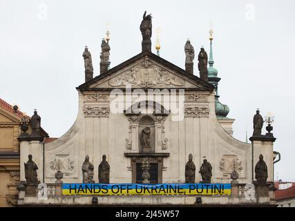 Banner 'Hands off Ukraine, Putin!' placed on the main facade of the Church of the Holy Saviour (Kostel Nejsvětějšího Salvátora) next to the Charles Bridge in Prague, Czech Republic, pictured on 2 April 2022. The banner in the colours of the Ukrainian national flag was hung on the Baroque church to protest against the Russian invasion of Ukraine in 2022. Stock Photo