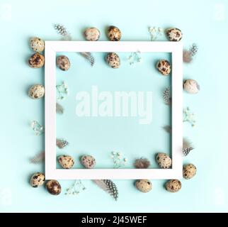 Frame of white square frame with quail eggs, feathers, white gypsophila flowers on light blue background. Easter greeting card. Easter decorations ide Stock Photo