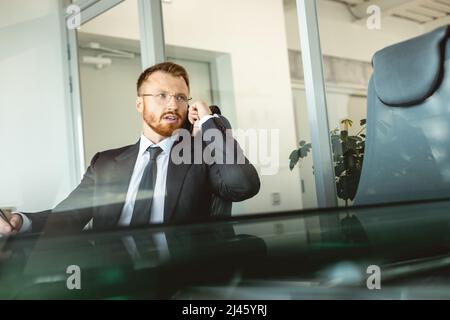 The head of the company is sitting at a table in the office in a business suit and glasses and talking on the phone. The role of a leader and manager Stock Photo