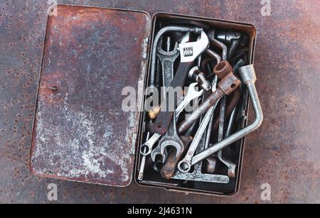 Open old toolbox of different dirty hand tools on rusty metal table. Top view Stock Photo