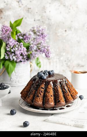 Chocolate cake decorated with frosting and berries on white textured background, spring composition with lilac flowers Stock Photo