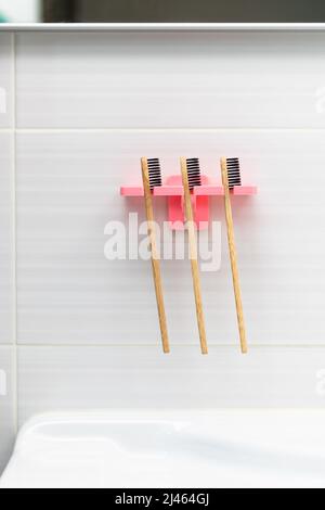 Three natural bamboo toothbrushes with black bristles in a holder against a tile background on the bathroom wall above the washbasin. Selective focus. Stock Photo