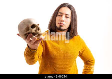 Young Caucasian bearded man holds skull and looks at it white background studio shot isolated . High quality photo Stock Photo