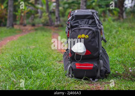 Traveling after pandemic, a backpack kept in mid of forest with a face mask hanging on it. Stock Photo