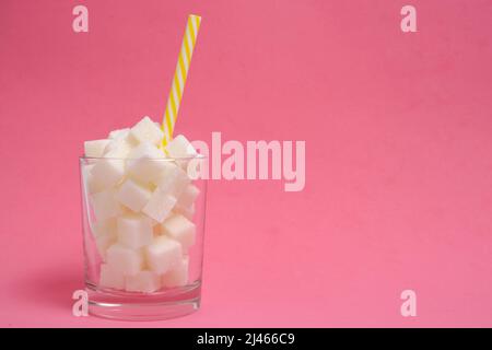 Glass with refined sugar cubes and a drinking tube on a pink background Stock Photo