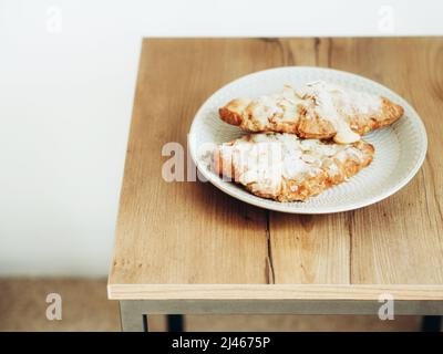 Traditional French breakfast croissant with almonds on plate on wood table Stock Photo