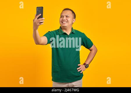 Cheerful young Asian man taking a selfie with a mobile phone on yellow background Stock Photo