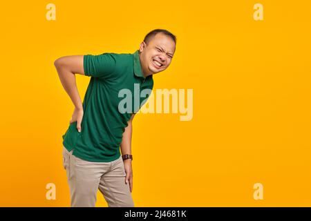 Portrait of handsome asian man suffering from back pain and touching back with hands on yellow background Stock Photo