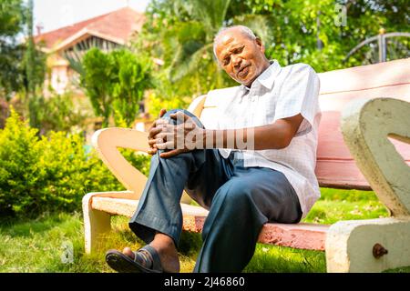 Senior old man suffering from knee joint pain while sitting at park - conept of arthritis, healthcare and injury Stock Photo
