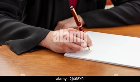 Woman holding a pen on a blank white paper, close up view, wooden office table background. Female hand signing on empty document, copy space Stock Photo