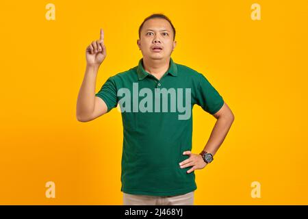Surprised young Asian man pointing up and having an idea on yellow background Stock Photo