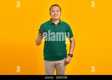 Portrait of smiling young Asian man holding mobile phone on yellow background Stock Photo
