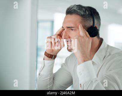 Come on, think. Shot of a mature customer service agent sitting alone in the office and looking contemplative while using his computer. Stock Photo
