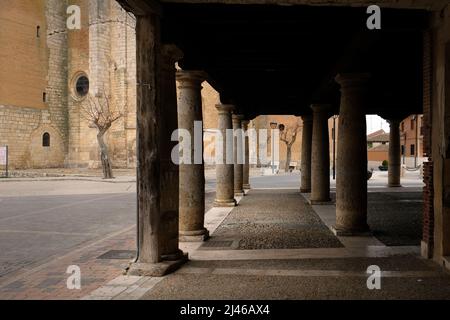 Looking though the pillars of the piered buildings in Plaza Mayor, Becerril de Campos, Spain, towards the Iglesia Parroquial de Santa Eugenia Stock Photo