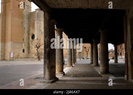 Looking though the pillars of the piered buildings in Plaza Mayor, Becerril de Campos, Spain, towards the Iglesia Parroquial de Santa Eugenia Stock Photo