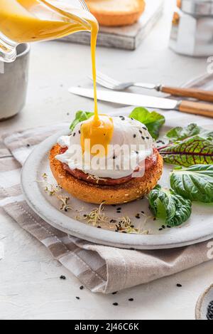 Pouring Hollandaise sauce over poached egg for cooking benedict egg for tasty breakfast. vertical orientation. English brunch Stock Photo