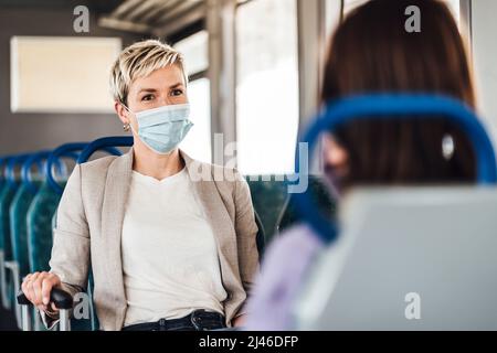 A couple of friends wearing mask and nicely talking while traveling by train Stock Photo