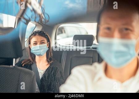 A woman wearing a protective mask sitting on the back seat of a taxi car Stock Photo