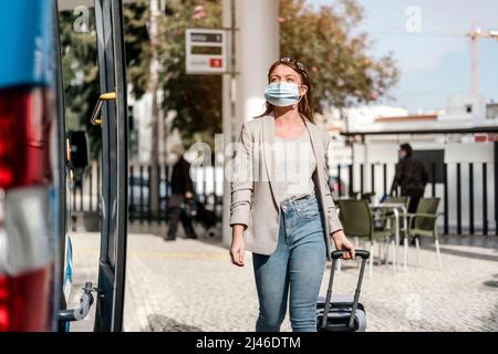 A young woman wearing protective maedical mask boarding the bus with a luggage Stock Photo