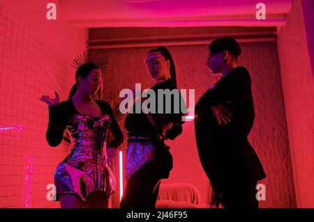 Three youthful performers in posh apparel performing vogue dance in modern night club while standing in front of camera Stock Photo