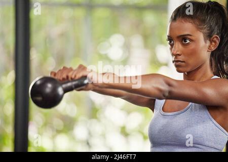 Keep doing it until you see results. Shot of a young woman working out with a kettle bell at the gym. Stock Photo