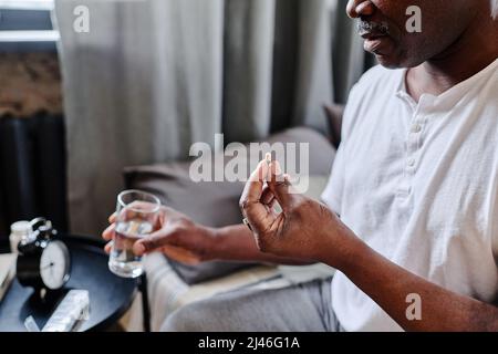 Contemporary senior African American man in white t-shirt taking sleeping pill before going to bed in the evening Stock Photo