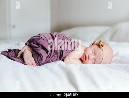 newborn baby girl covered in a swaddle laying on a white bed Stock Photo