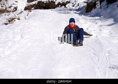 Boy slides down from the snow slope. Enjoying the winter sledding time Stock Photo