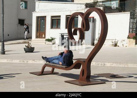 Alberobello, Italy. Man sitting on a heart-shaped bench in the center of tthe city. Stock Photo