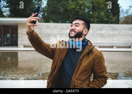 Cheerful asian man in outerwear taking selfie on smartphone Stock Photo