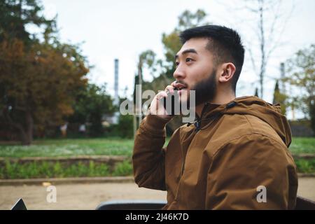Asian man talking on smartphone in city park Stock Photo