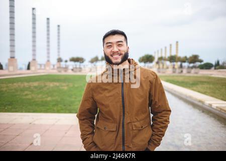 Smiling Asian man standing in park on cloudy day Stock Photo