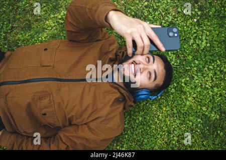 Joyful ethnic man in headphones taking selfie on smartphone Stock Photo