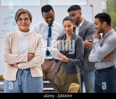 Leading her team towards greatness. Portrait of a mature businesswoman standing with her arms crossed in an office with her colleagues in the Stock Photo
