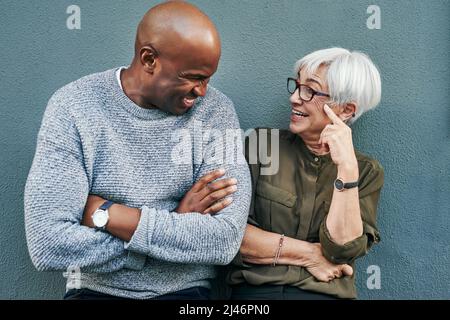 Its always good vibes when were together. Shot of two cheerful mature businesspeople having a discussion while standing against a wall outdoors. Stock Photo