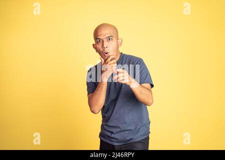 amazed asian bald man with hand holding mouth and pointing Stock Photo