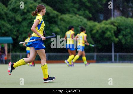 Young teenage girl running on the pitch during the field hockey game in rain Stock Photo