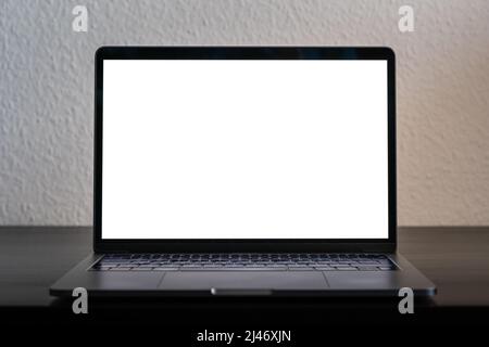 Empty laptop screen perfect for testing and a mockup of a design. Bright white screen in a dark environment. Device standing on a black wooden desk. Stock Photo